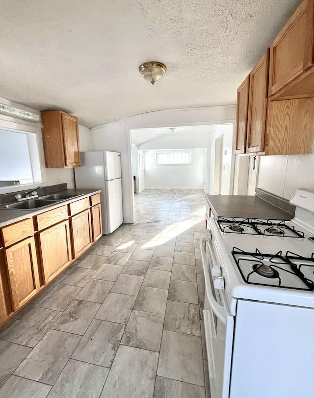 kitchen featuring a textured ceiling, sink, vaulted ceiling, and white appliances