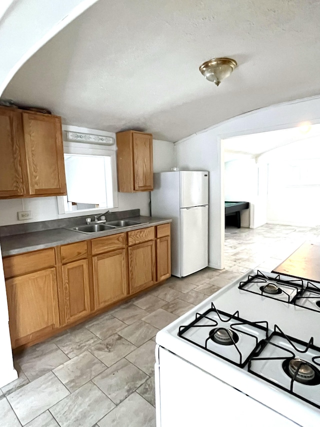 kitchen featuring a textured ceiling, lofted ceiling, white appliances, and sink