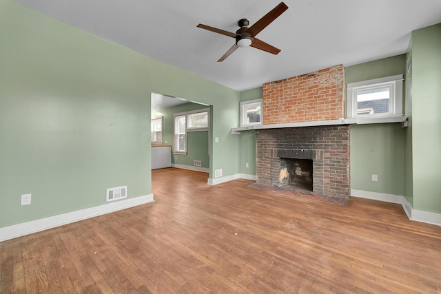 unfurnished living room with ceiling fan, wood-type flooring, and a brick fireplace