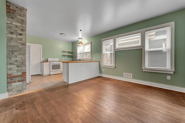 interior space with white range with gas cooktop, sink, kitchen peninsula, and light wood-type flooring