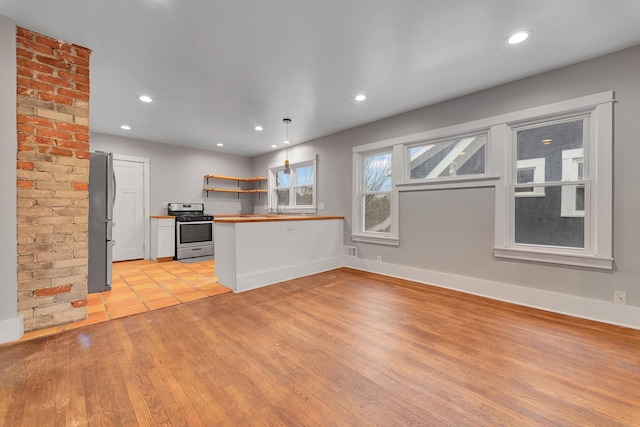 kitchen with kitchen peninsula, light wood-type flooring, appliances with stainless steel finishes, decorative light fixtures, and butcher block counters