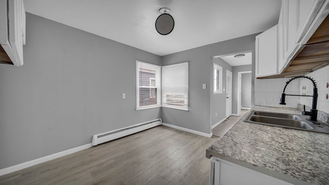 kitchen with backsplash, a baseboard heating unit, sink, light hardwood / wood-style flooring, and white cabinets