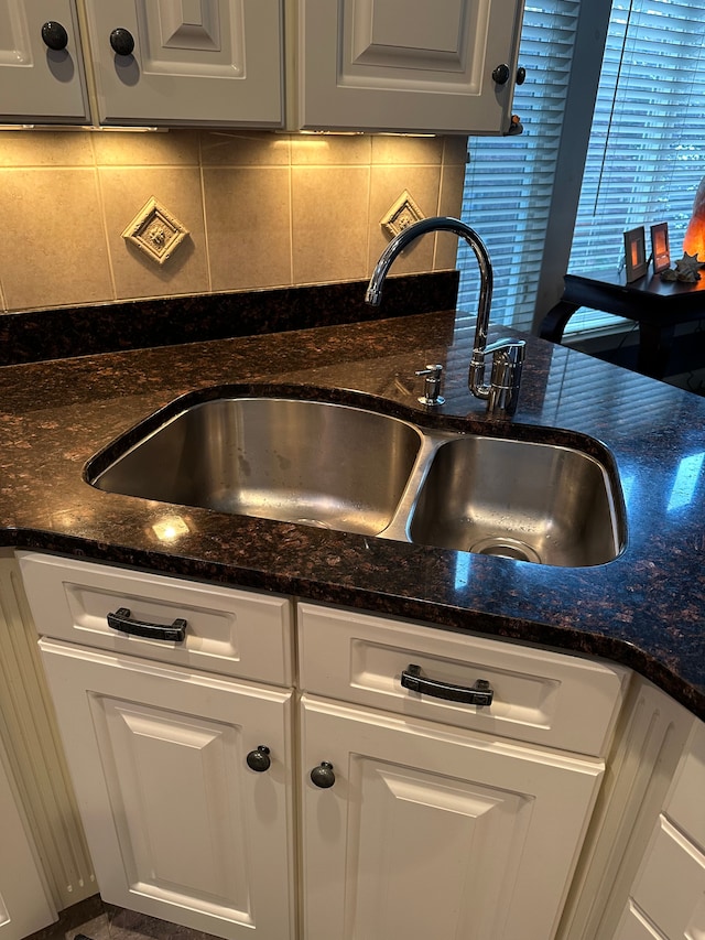 room details with decorative backsplash, dark stone countertops, white cabinetry, and sink