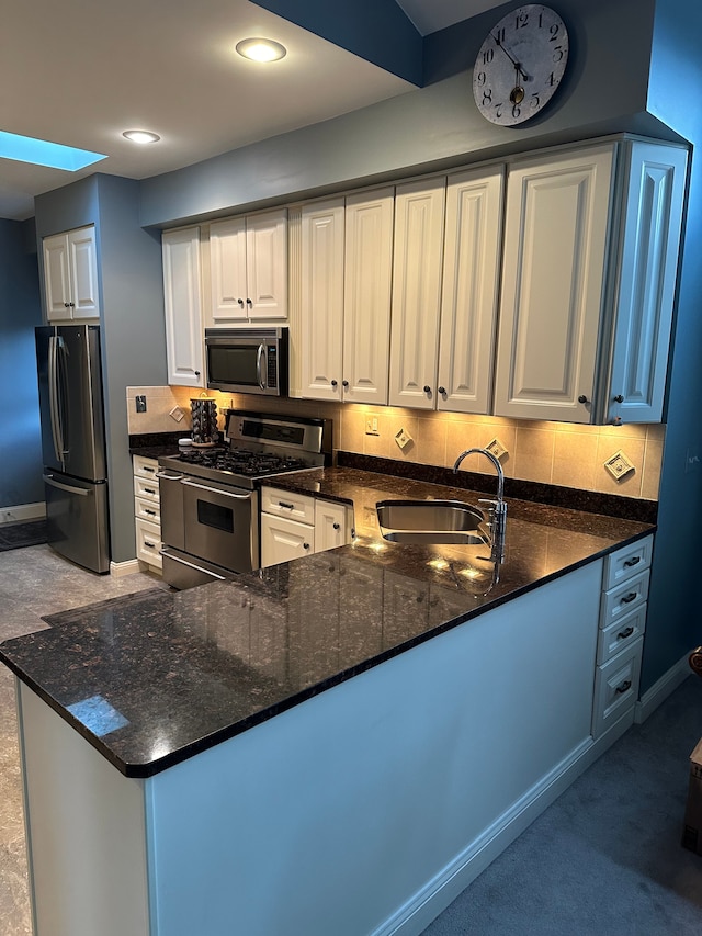 kitchen with dark stone counters, sink, white cabinetry, kitchen peninsula, and stainless steel appliances