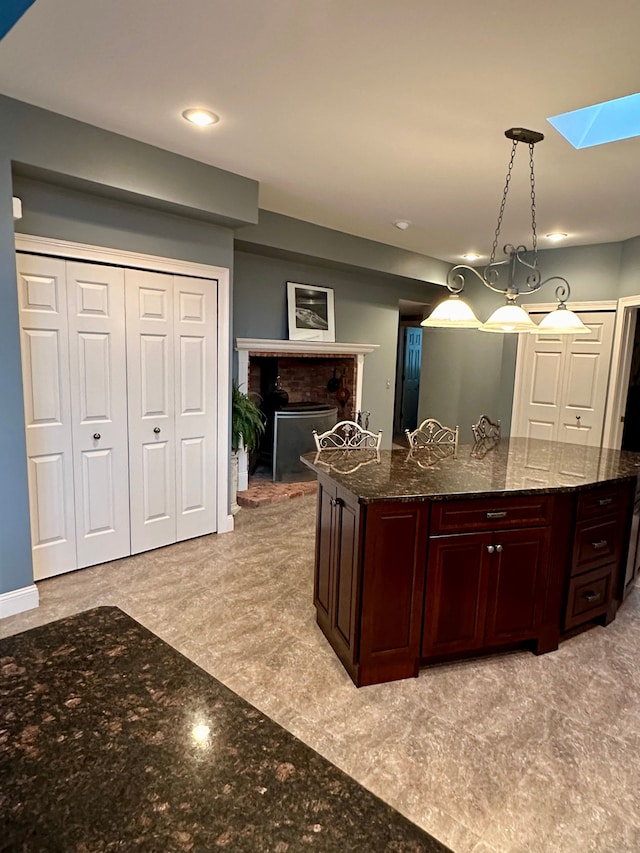 kitchen featuring dark stone counters, a skylight, a fireplace, and pendant lighting