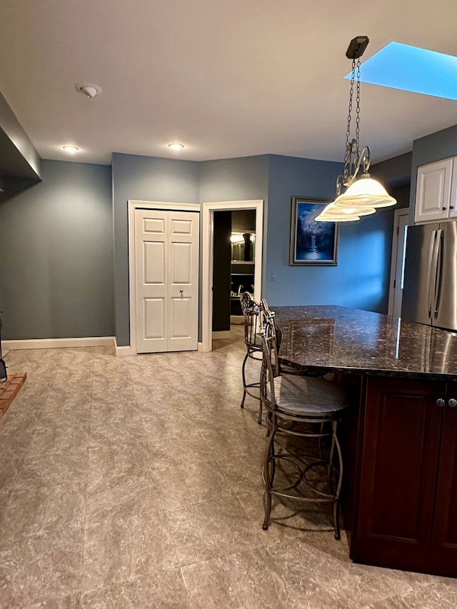 kitchen featuring stainless steel refrigerator, hanging light fixtures, a breakfast bar area, and dark stone countertops