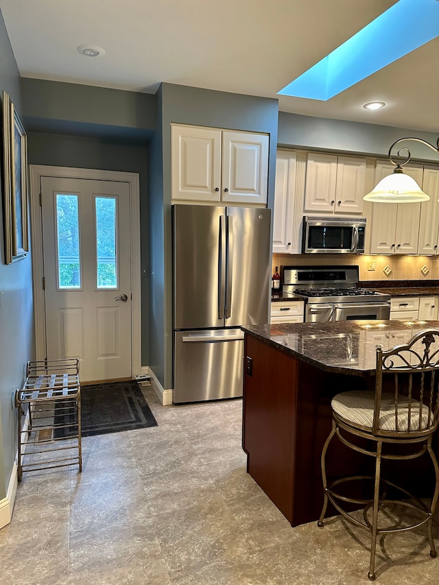 kitchen with a breakfast bar, stainless steel appliances, a skylight, and dark stone counters