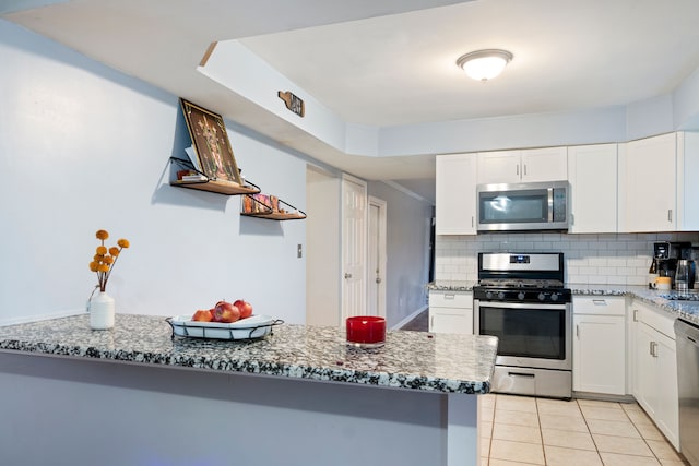 kitchen with kitchen peninsula, tasteful backsplash, stainless steel appliances, stone countertops, and white cabinets