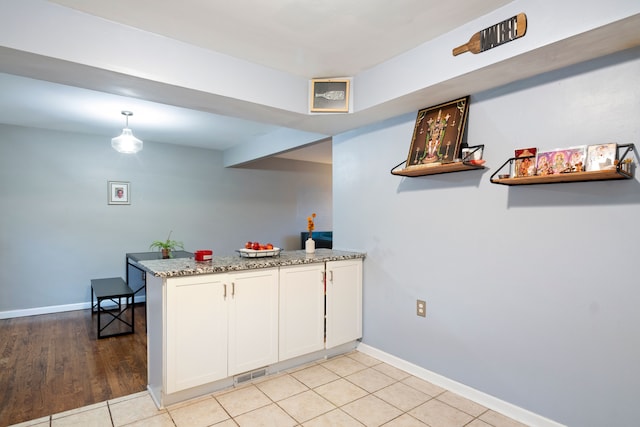 kitchen with kitchen peninsula, light stone counters, decorative light fixtures, white cabinets, and light hardwood / wood-style floors