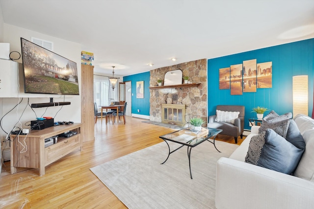 living room with a stone fireplace, light wood-type flooring, and an inviting chandelier