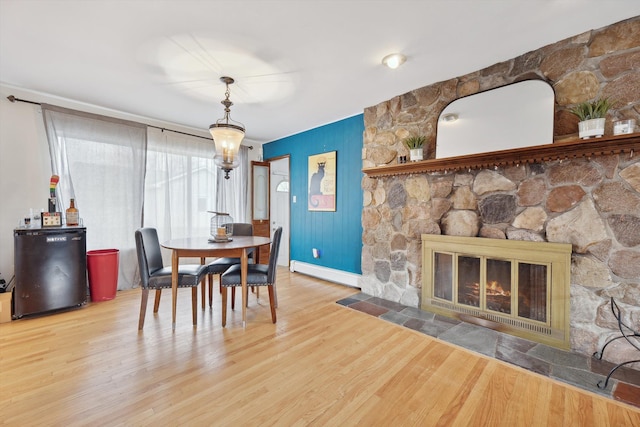 dining space featuring baseboard heating, a stone fireplace, and hardwood / wood-style flooring