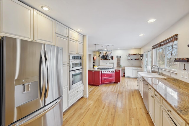 kitchen with sink, light hardwood / wood-style flooring, pendant lighting, cream cabinetry, and appliances with stainless steel finishes