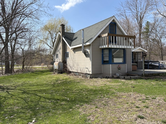view of side of property with a yard, heating fuel, a balcony, a chimney, and a shingled roof