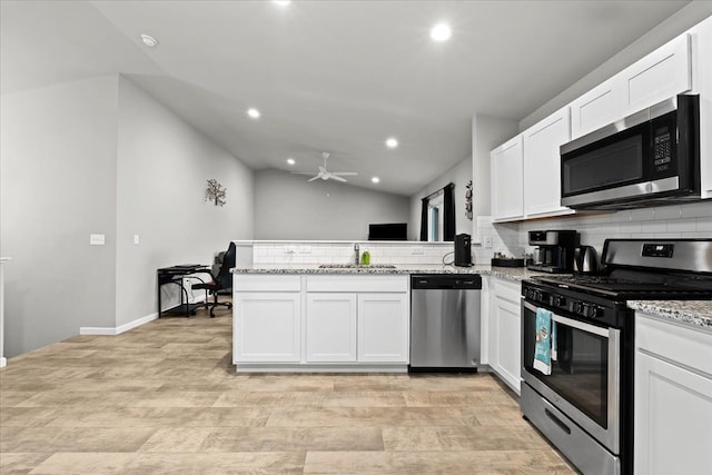 kitchen with kitchen peninsula, stainless steel appliances, vaulted ceiling, sink, and white cabinets