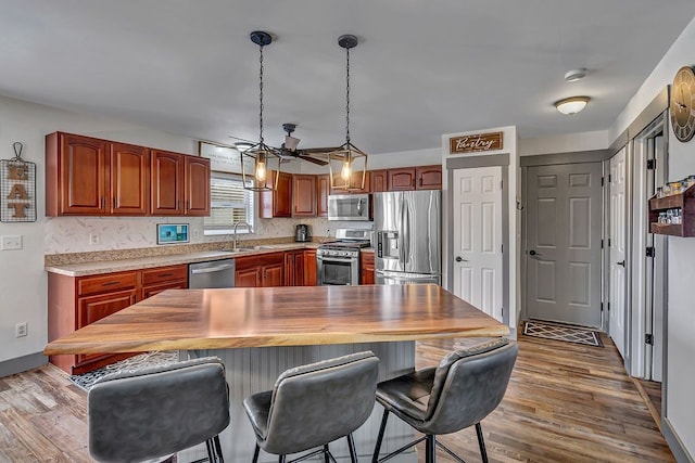 kitchen featuring ceiling fan, sink, stainless steel appliances, decorative light fixtures, and hardwood / wood-style flooring