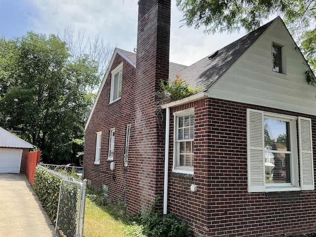 view of home's exterior with brick siding, a shingled roof, fence, a chimney, and an outbuilding