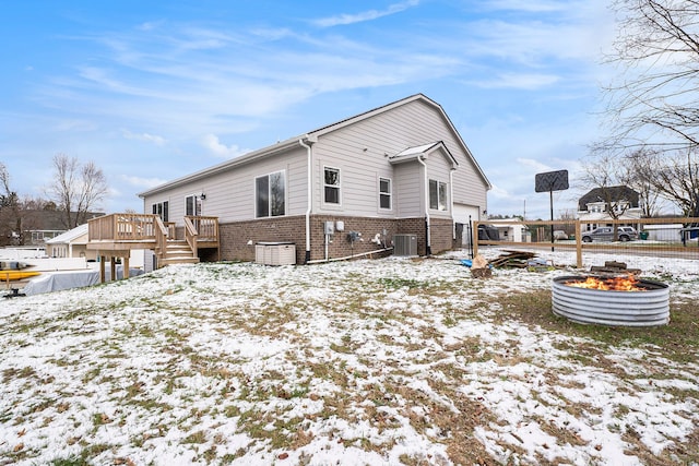 snow covered property with a wooden deck, central AC, and an outdoor fire pit