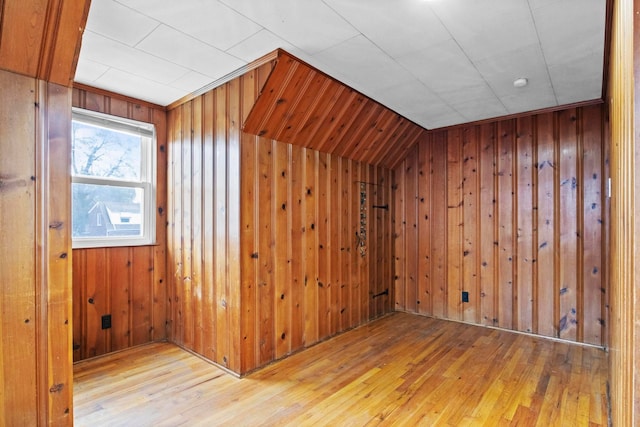 additional living space with wood walls, lofted ceiling, and light hardwood / wood-style flooring