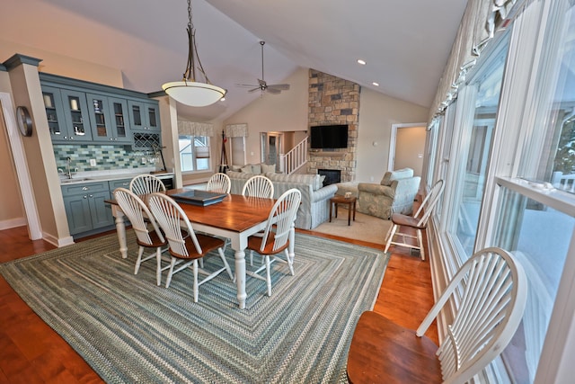 dining room featuring ceiling fan, sink, hardwood / wood-style flooring, high vaulted ceiling, and a fireplace