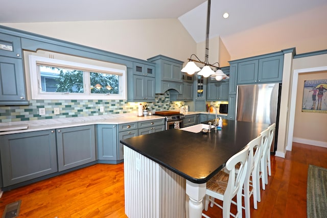 kitchen with stainless steel appliances, sink, a center island with sink, hanging light fixtures, and lofted ceiling