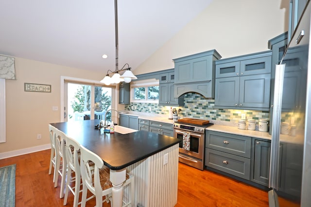 kitchen with a kitchen breakfast bar, high end stove, sink, hardwood / wood-style floors, and an island with sink