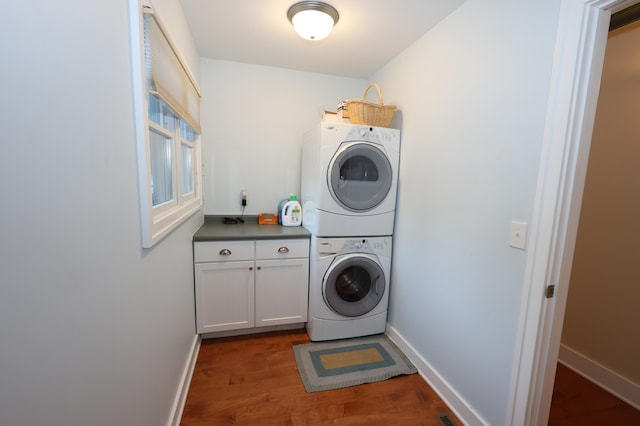 laundry room with cabinets, wood-type flooring, and stacked washer and clothes dryer