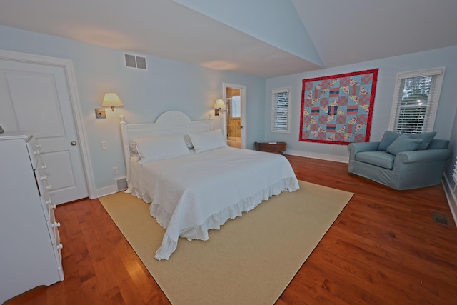 bedroom with hardwood / wood-style floors, lofted ceiling, and connected bathroom