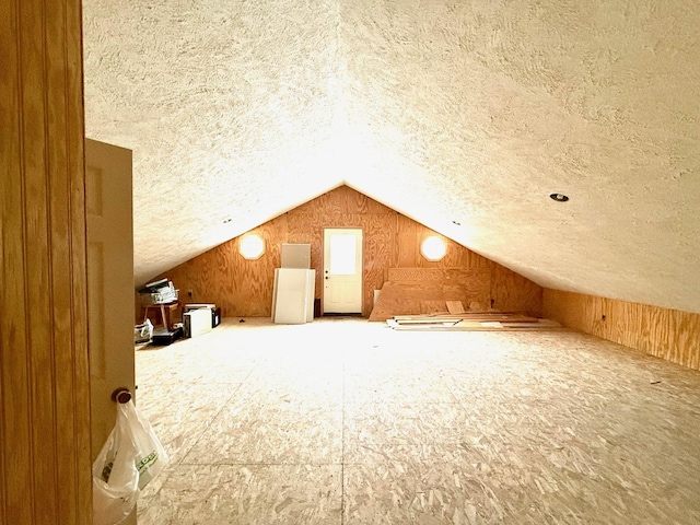 bonus room featuring vaulted ceiling, a textured ceiling, and wood walls