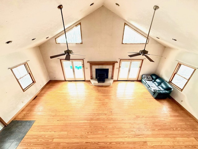 unfurnished living room featuring ceiling fan, a tile fireplace, high vaulted ceiling, and light hardwood / wood-style flooring