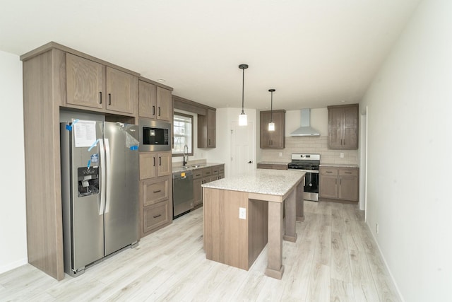 kitchen with wall chimney exhaust hood, stainless steel appliances, decorative light fixtures, light hardwood / wood-style flooring, and a center island