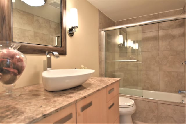 full bathroom with enclosed tub / shower combo, vanity, and toilet