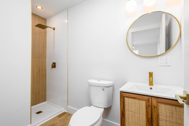 bathroom with a tile shower, hardwood / wood-style floors, vanity, and toilet