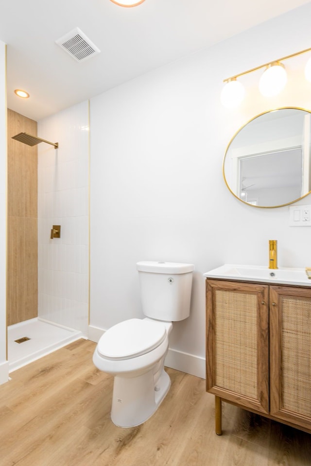 bathroom with toilet, vanity, wood-type flooring, and tiled shower