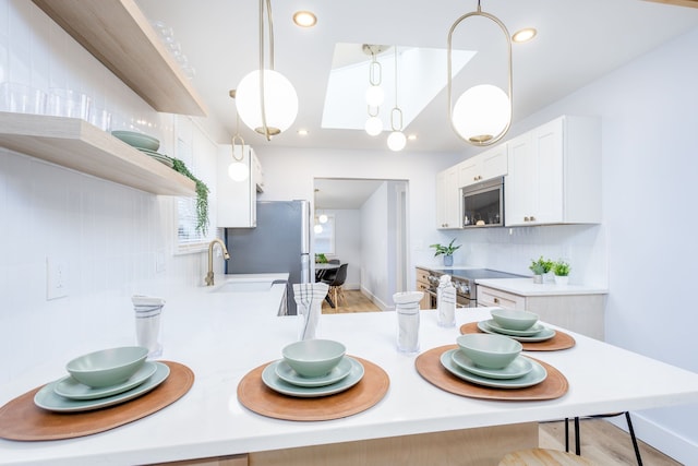 kitchen with appliances with stainless steel finishes, tasteful backsplash, sink, pendant lighting, and white cabinets