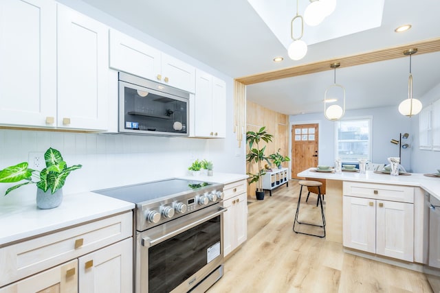 kitchen featuring appliances with stainless steel finishes, decorative light fixtures, white cabinetry, and light hardwood / wood-style flooring