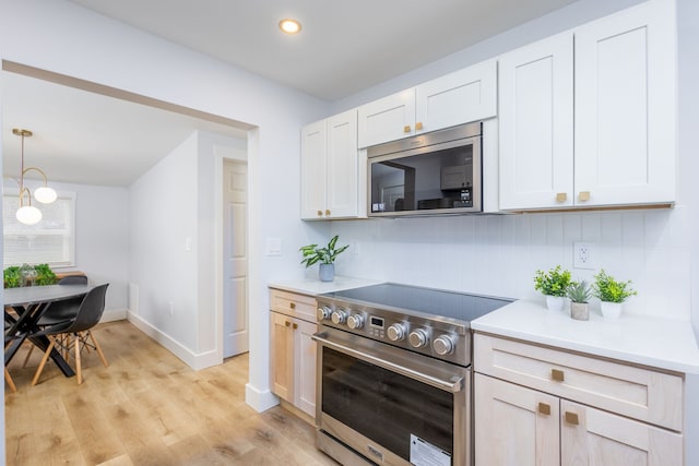 kitchen featuring backsplash, white cabinets, hanging light fixtures, light wood-type flooring, and appliances with stainless steel finishes