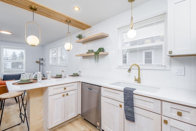 kitchen featuring sink, hanging light fixtures, stainless steel dishwasher, light wood-type flooring, and kitchen peninsula