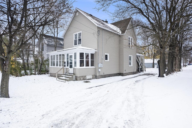 snow covered back of property featuring a sunroom