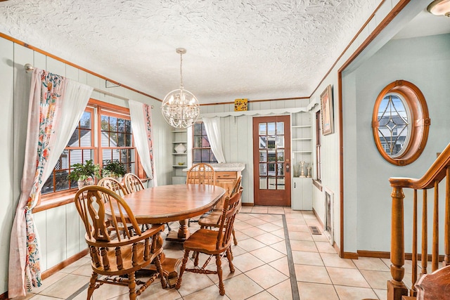 tiled dining space featuring a notable chandelier, ornamental molding, a textured ceiling, and built in shelves