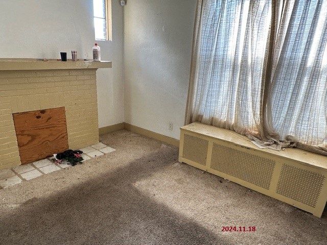 unfurnished living room featuring light colored carpet, radiator heating unit, and a fireplace