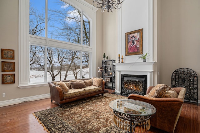 living room with a high ceiling, wood finished floors, baseboards, and a warm lit fireplace