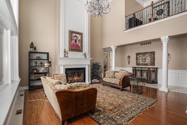 living room with a chandelier, hardwood / wood-style floors, ornate columns, and a high ceiling