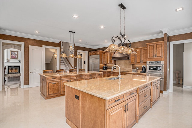 kitchen featuring brown cabinetry, a warm lit fireplace, stainless steel appliances, a sink, and a large island