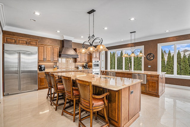 kitchen with a large island, custom range hood, appliances with stainless steel finishes, brown cabinets, and a wealth of natural light