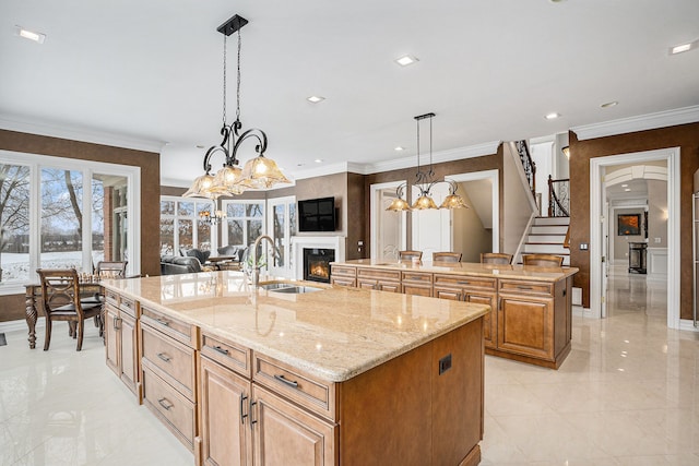 kitchen featuring a sink, light stone counters, open floor plan, a lit fireplace, and a large island with sink