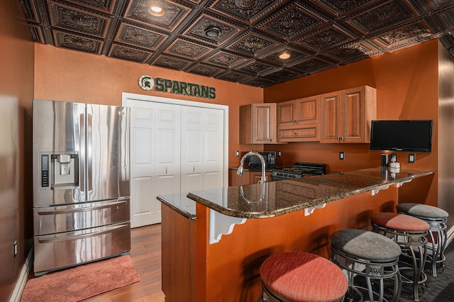 kitchen with stainless steel fridge with ice dispenser, kitchen peninsula, dark stone countertops, black gas stove, and hardwood / wood-style floors