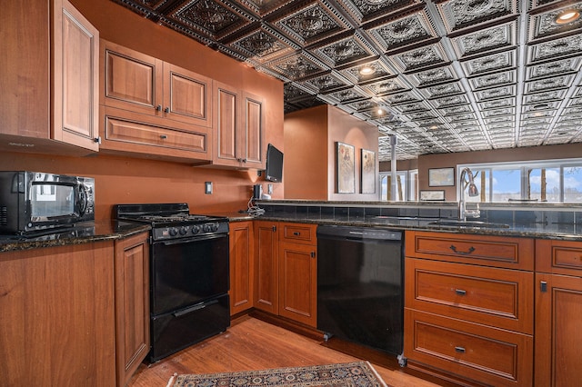 kitchen featuring dark stone counters, extractor fan, sink, black appliances, and light hardwood / wood-style flooring