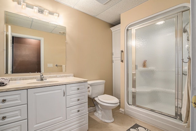 bathroom with a paneled ceiling, vanity, tile patterned flooring, toilet, and walk in shower