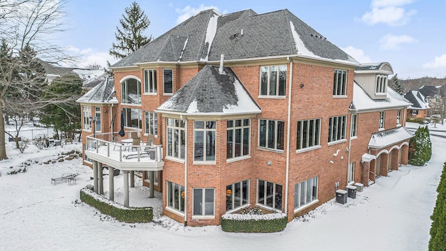 snow covered rear of property featuring brick siding and a shingled roof