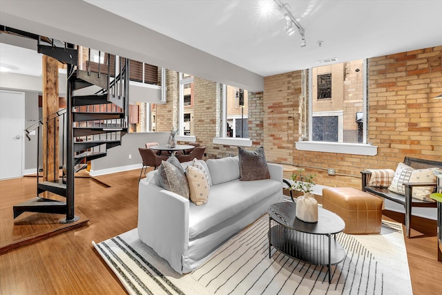 living room featuring rail lighting, light hardwood / wood-style floors, and brick wall